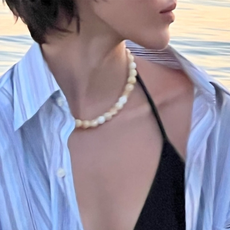 Model wearing black bikini, blue button-down shirt, and white stone necklace while at beach.