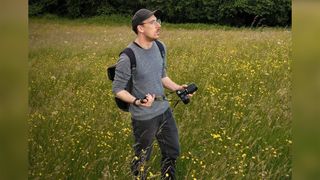 A man with a camera walking through a meadow