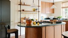 Image of a white kitchen with warm wooden cabinetry and a matching wooden kitchen island. There are teal marble countertops and a green pantry.