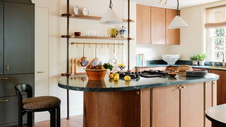 Image of a white kitchen with warm wooden cabinetry and a matching wooden kitchen island. There are teal marble countertops and a green pantry.