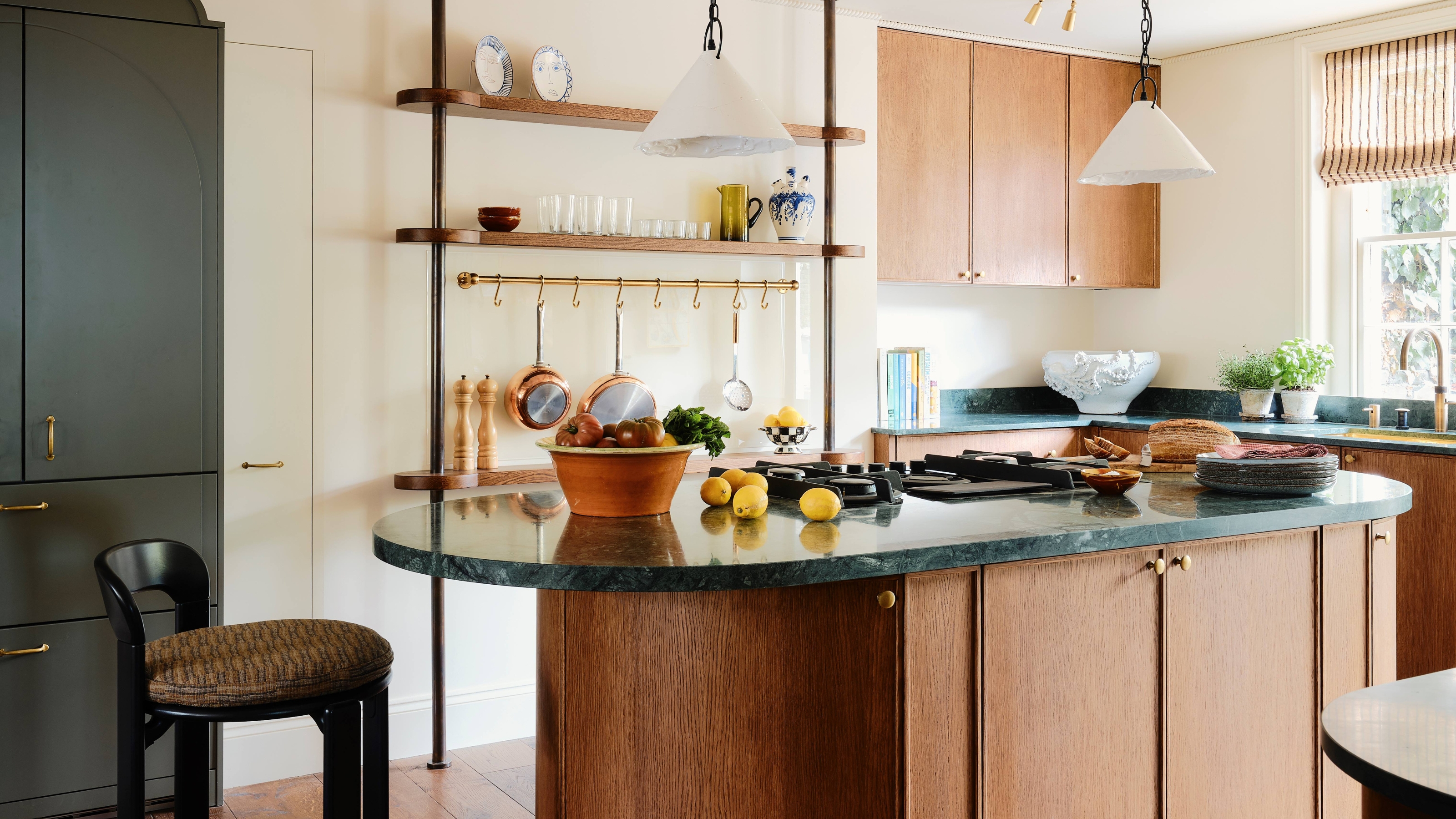 Image of a white kitchen with warm wooden cabinetry and a matching wooden kitchen island. There are teal marble countertops and a green pantry.