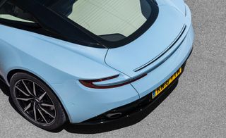 View of left back wheel and fender of light blue Aston Martin DB11 sports car
