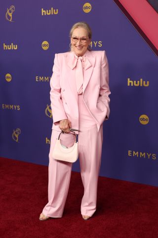 Meryl Streep wears a pink blazer, pink blouse, pink trousers, and a pink bag.