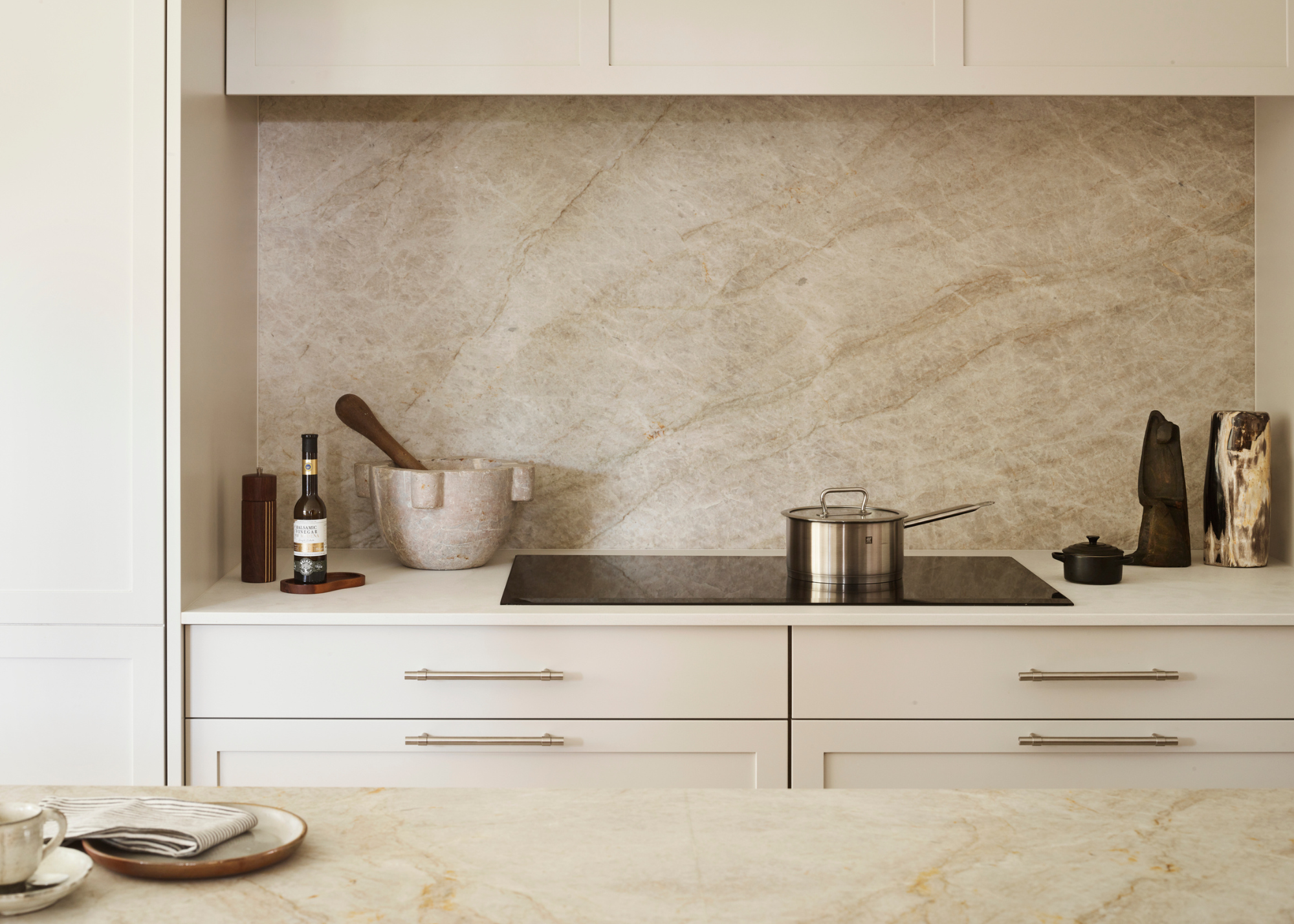 a beautiful modern kitchen with pale veined marble counters and backsplash and light neutral cabinetry