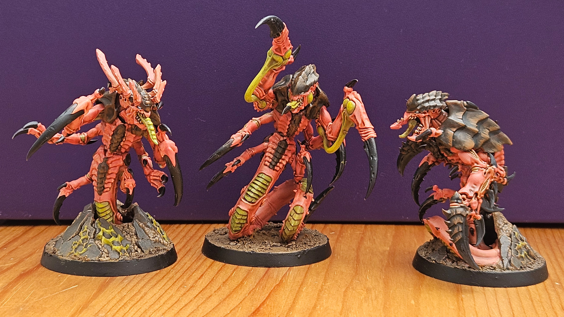 Three painted Tyranid Ravener models on a wooden surface, lined up against a purple background