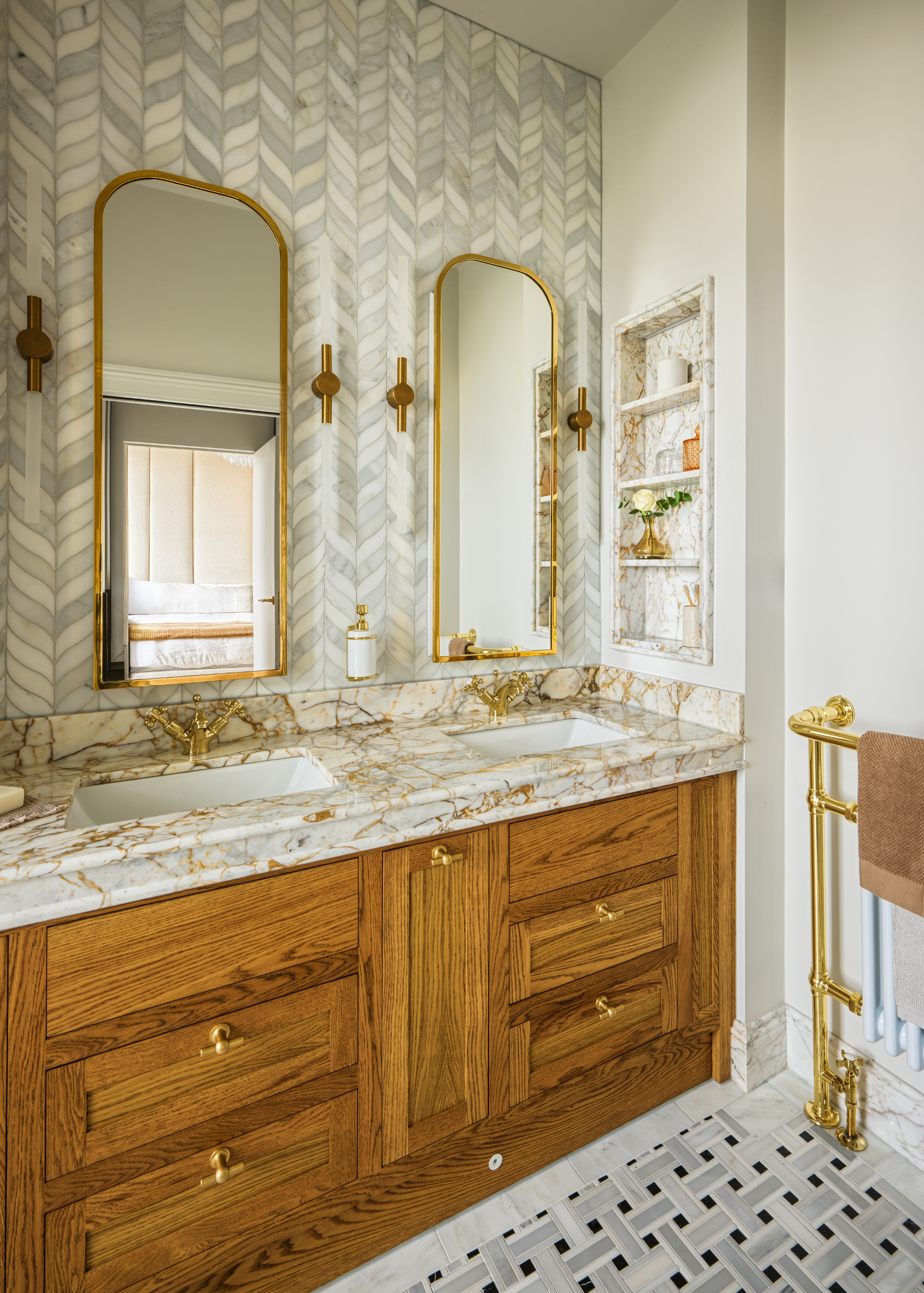 A modern traditional bathroom with a double wood vanity, a light marble top and pattern tiles on the flloor and wall.