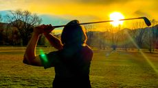 Female golfer hitting balls at the range into the sunset