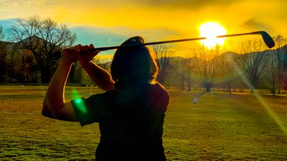Female golfer hitting balls at the range into the sunset