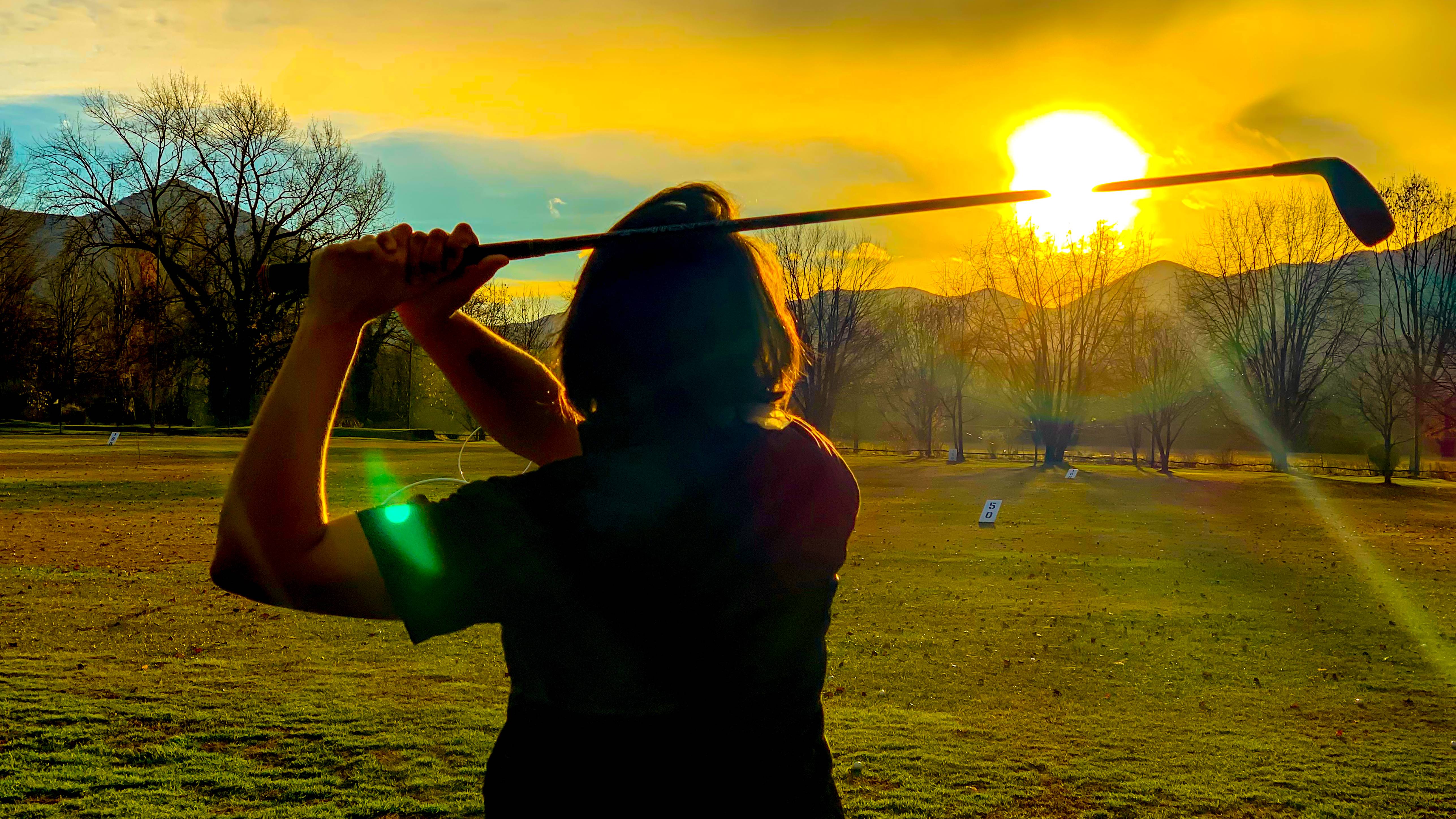 Female golfer hitting balls at the range into the sunset