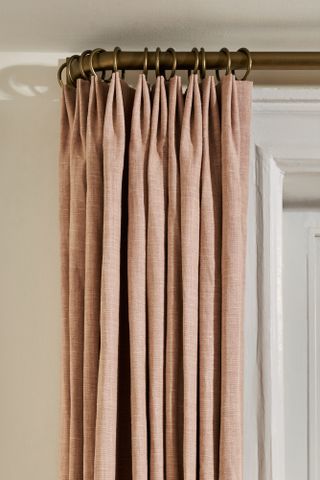 Close up of soft pink curtains with a brass pole and rings