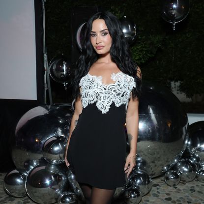 a woman with long, black hair wearing a black and white mini dress posing in front of silver balloons