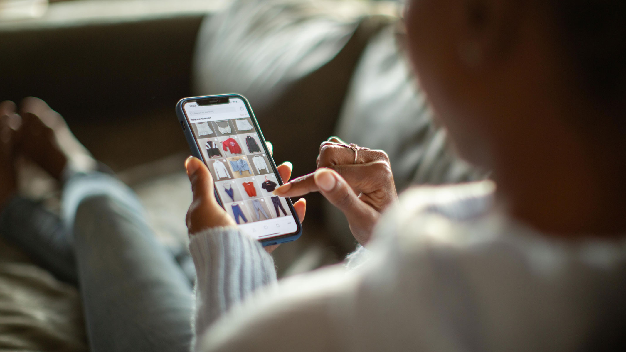 A close-up picture of a woman sitting on a couch and shopping for workout clothes on her mobile phone