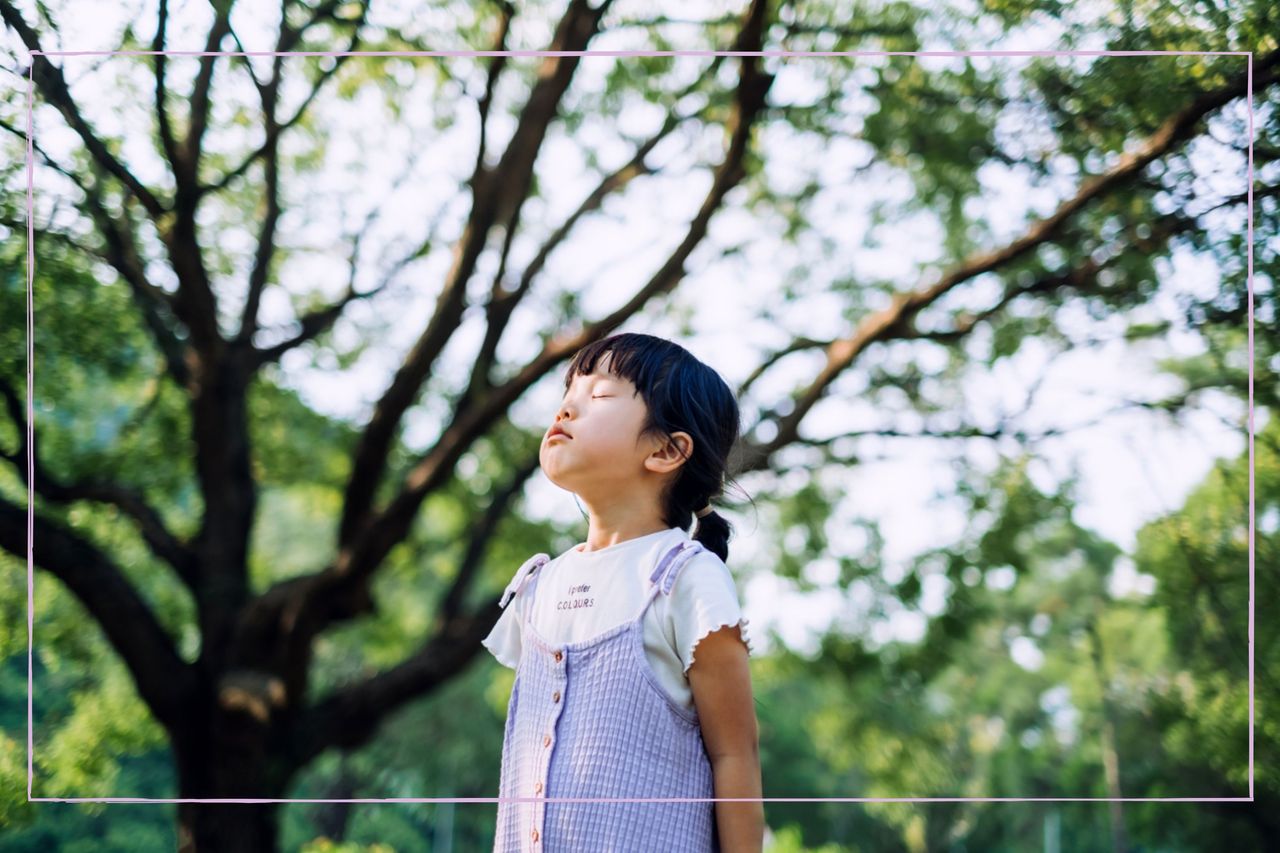 A young girl stood outside with her eyes closed