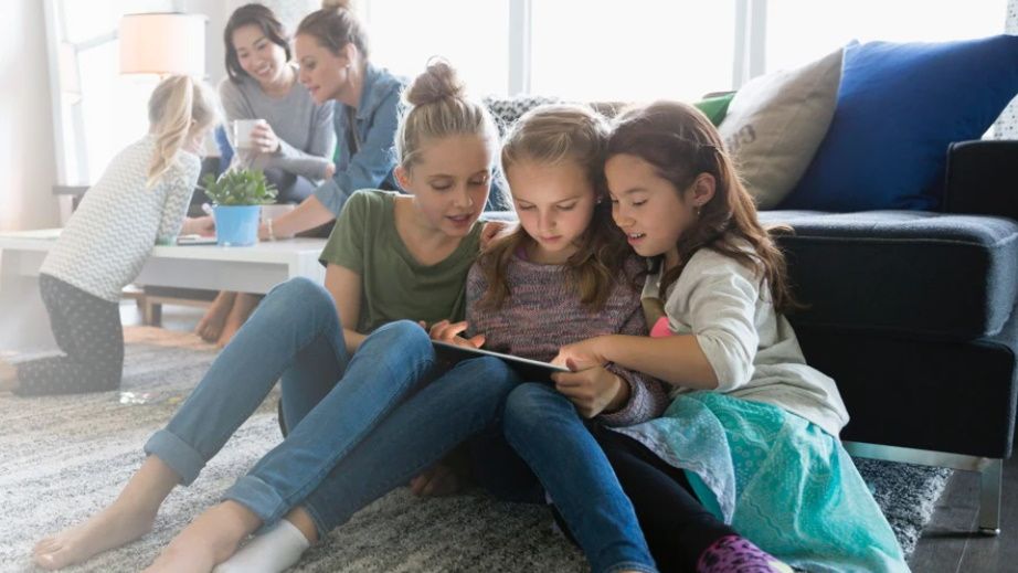 Children gathered around a tablet PC while parents are distracted in background