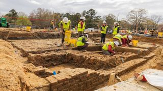 An excavation site with archaeologists working in hard hats