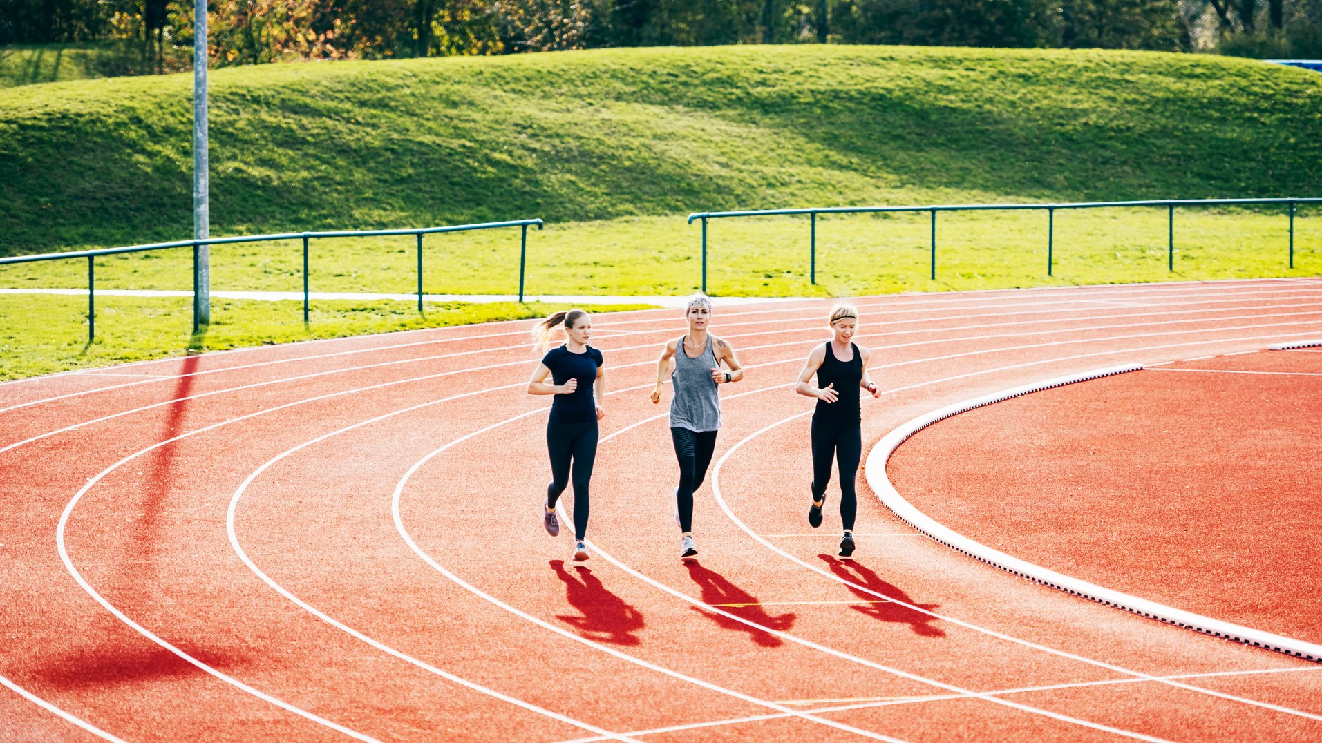 Three women run on a track in a sunny day