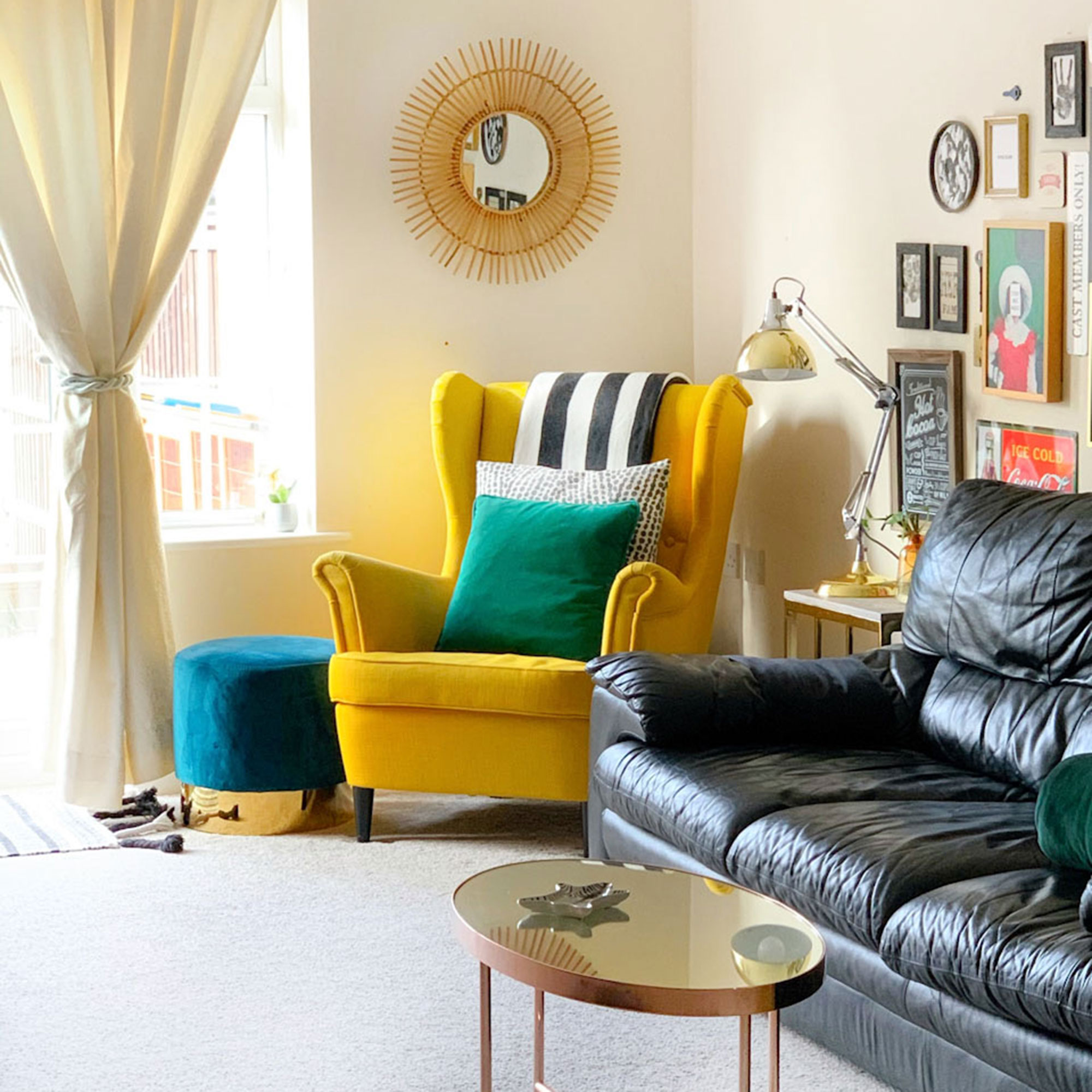 Neutral living room with yellow armchair, rattan mirror and leather sofa in front of gallery wall