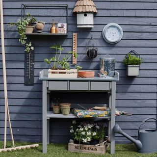 Blue potting bench in front of a blue cladded shed, covered in gardening accessories