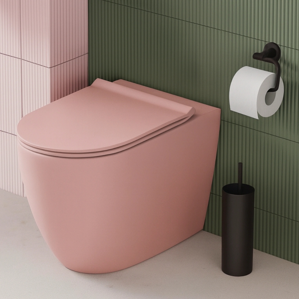 Matte pink toilet against ribbed green and pink tiles, black toilet brush and toilet roll holder beside.
