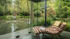 glass garden room with recliner and faux fur throw overlooking water garden and trees