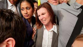 photo of woman in business casual on a crowded train; a man with sweaty armpits is holding the pole next to her and she's pulling a face of disgust