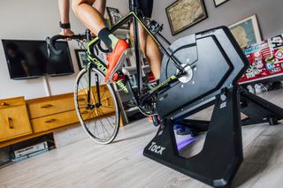 Wahoo RGT image shows the lower half of a rider on a bike mounted on a smart turbo trainer at home in front of a TV screen