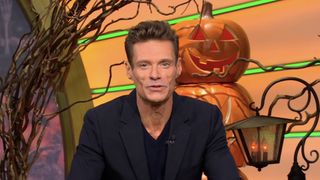 Ryan Seacrest wearing black with pumpkins behind him on Wheel of fortune.
