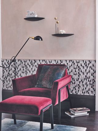 A living room corner with a bright pink velvet armchair and walls with half patterned pink and black wallpaper and half pink paint