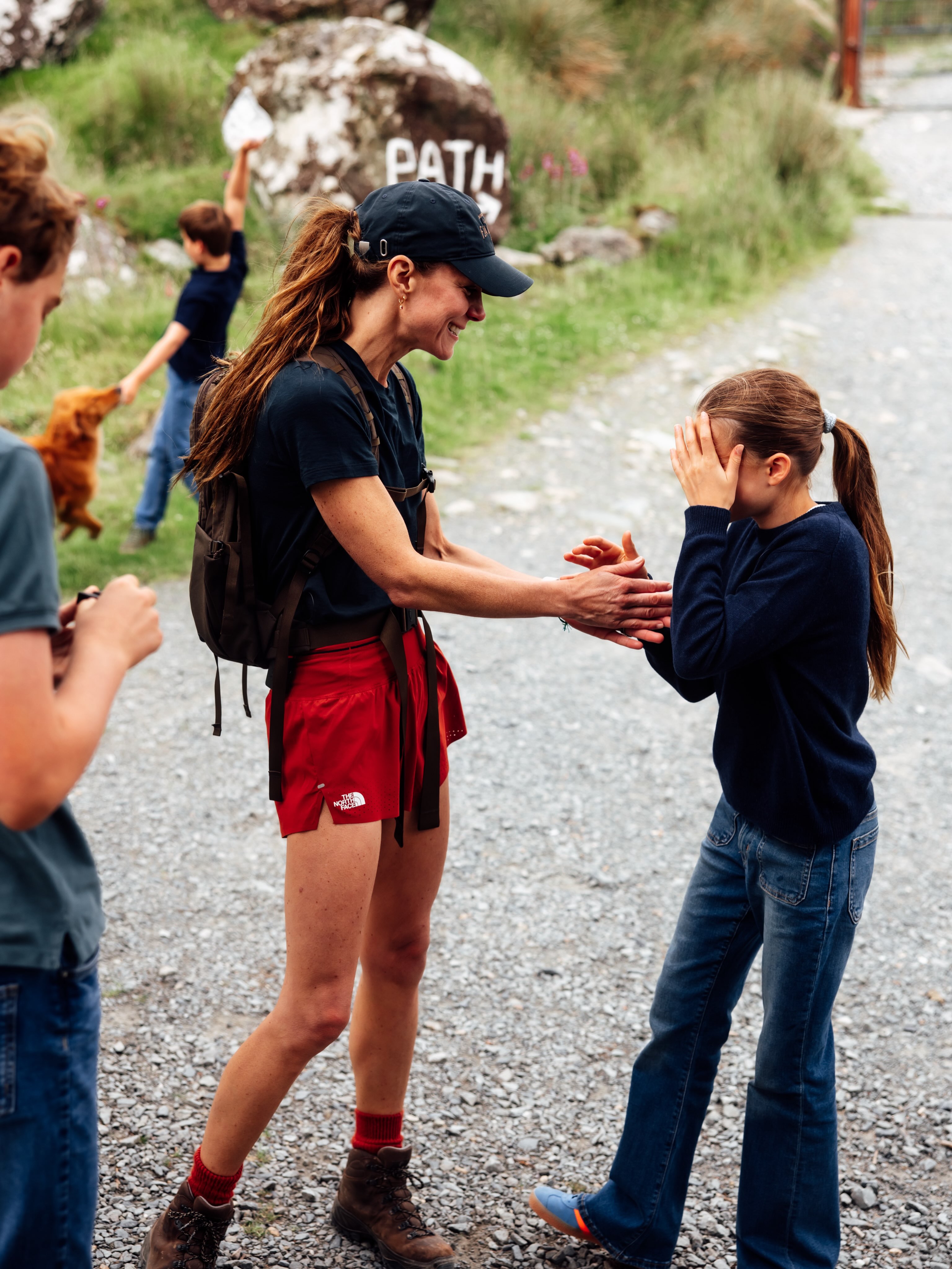 Princess Kate, wore is wearing red shorts and navy baseball cap, is greeted by her three children, Princess Charlotte, Prince George, and Prince Louis, who all wear matching denim jeans