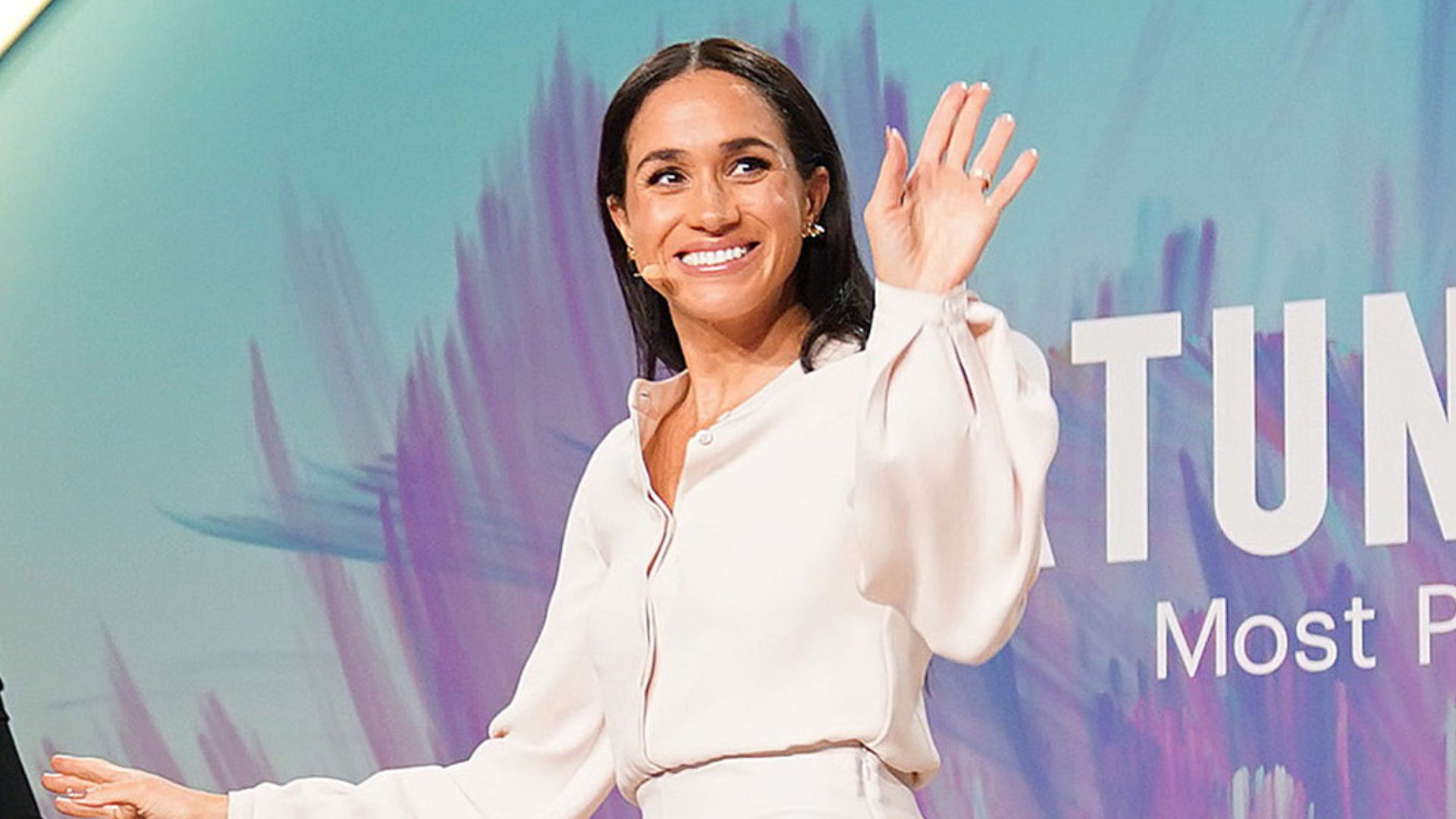 Meghan Markel walks off stage wearing a white pencil skirt and blouse with nude ankle strap heels.