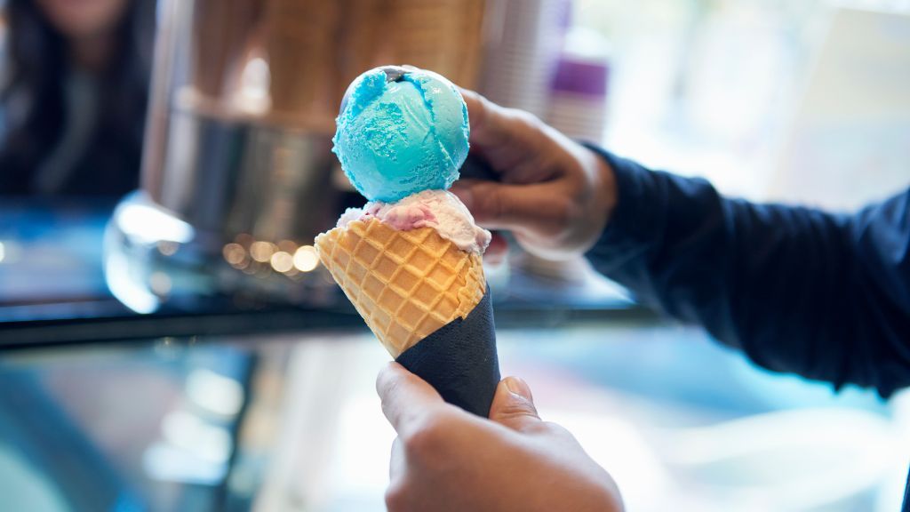 close-up of a man&#039;s hands as he scoops a second scoop of ice cream into a waffle cone