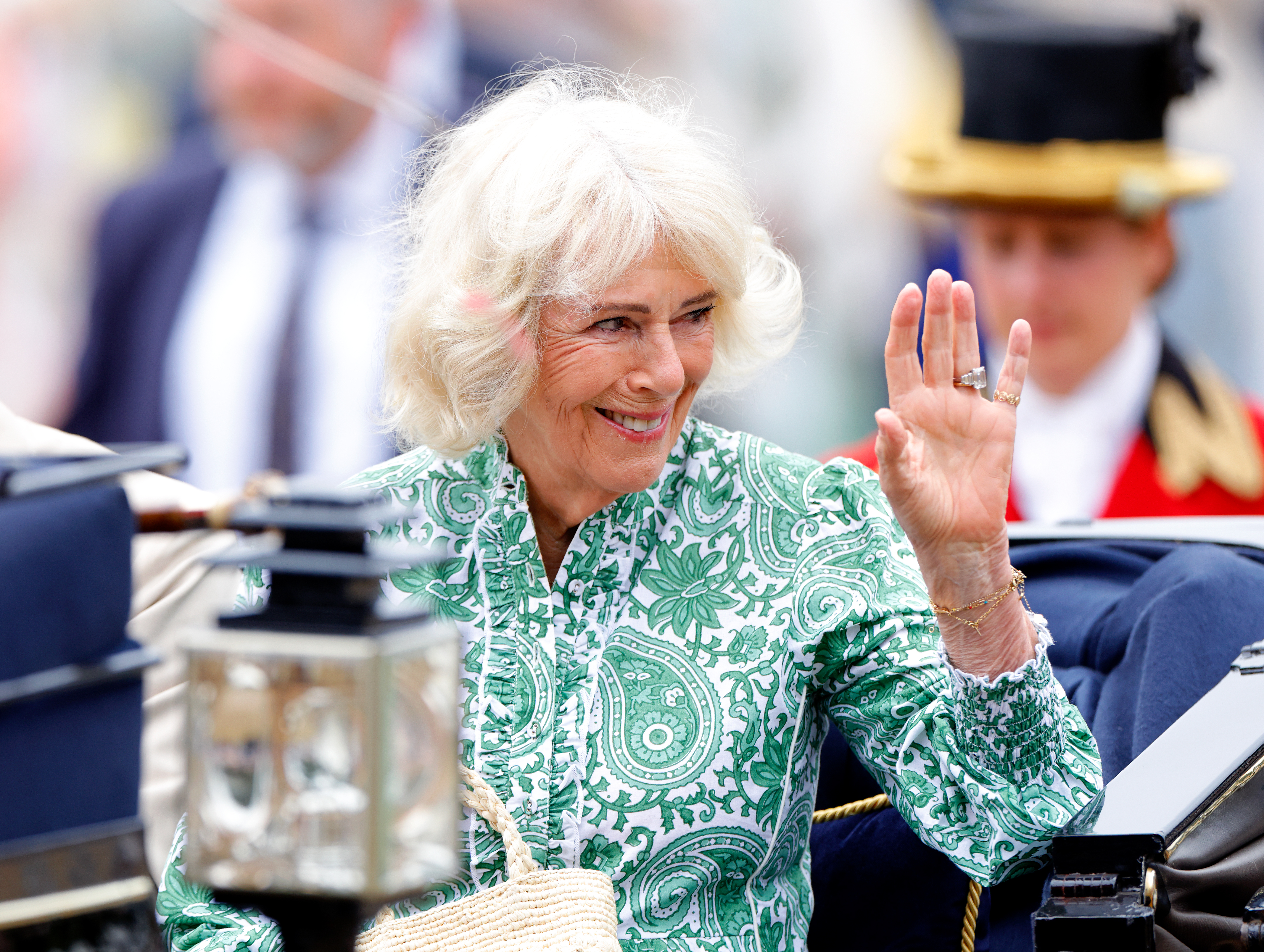 Queen Camilla wearing a green dress waving from a carriage