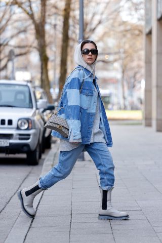 Influencer Nadine Tosun wearing a blue patchwork denim jeans jacket by Topshop, blue denim jeans pants by Isabel Marant, a grey pullover by Edited, a grey Balaclava by Nadine Tosun the Label, grey boots by Copenhagen Studios, a grey bag by Balenciaga ans sunglasses by The Attico during a street style shooting on January 27, 2022 in Munich, Germany.