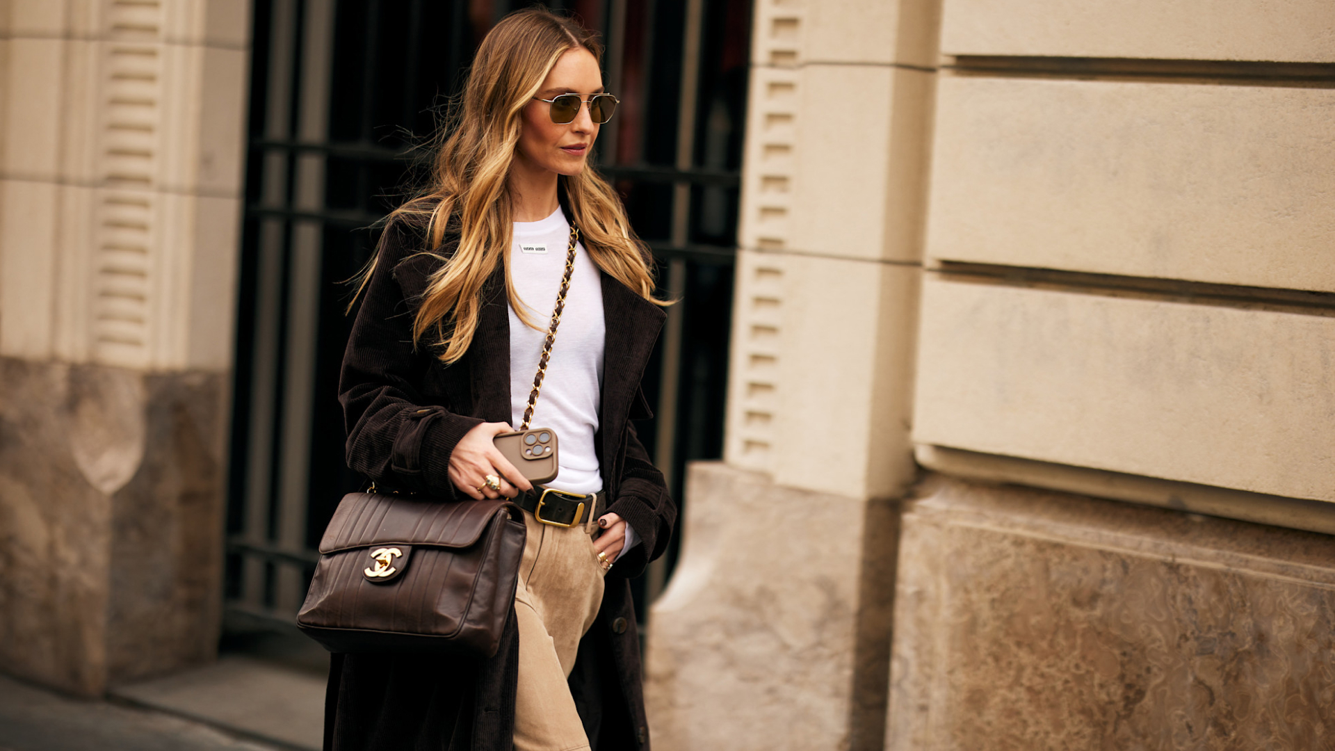 Fashion week attendee wearing sunglasses, white shirt, long coat, and brown chanel crossbody bag