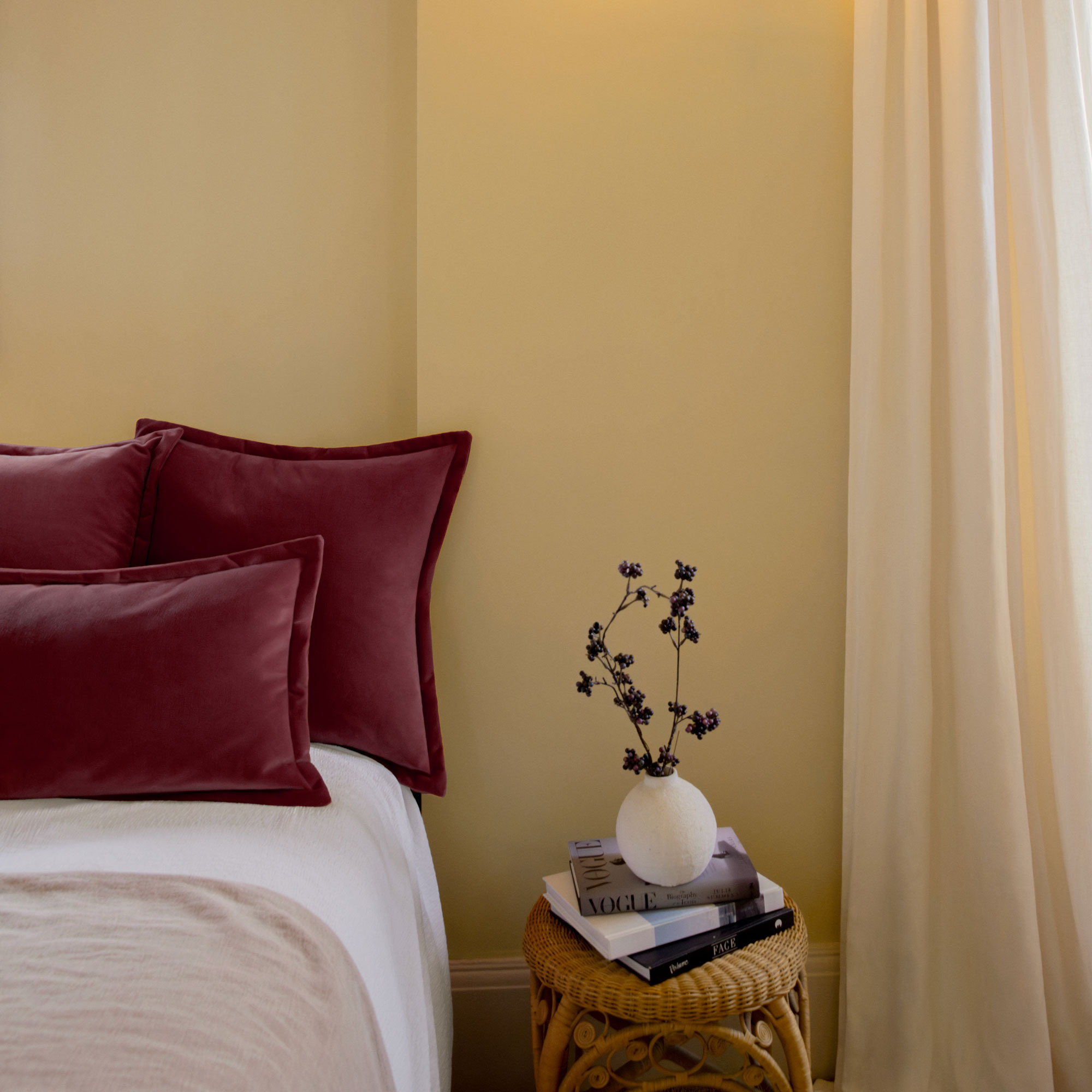 Yellow bedroom with rattan side table and velvet cushions