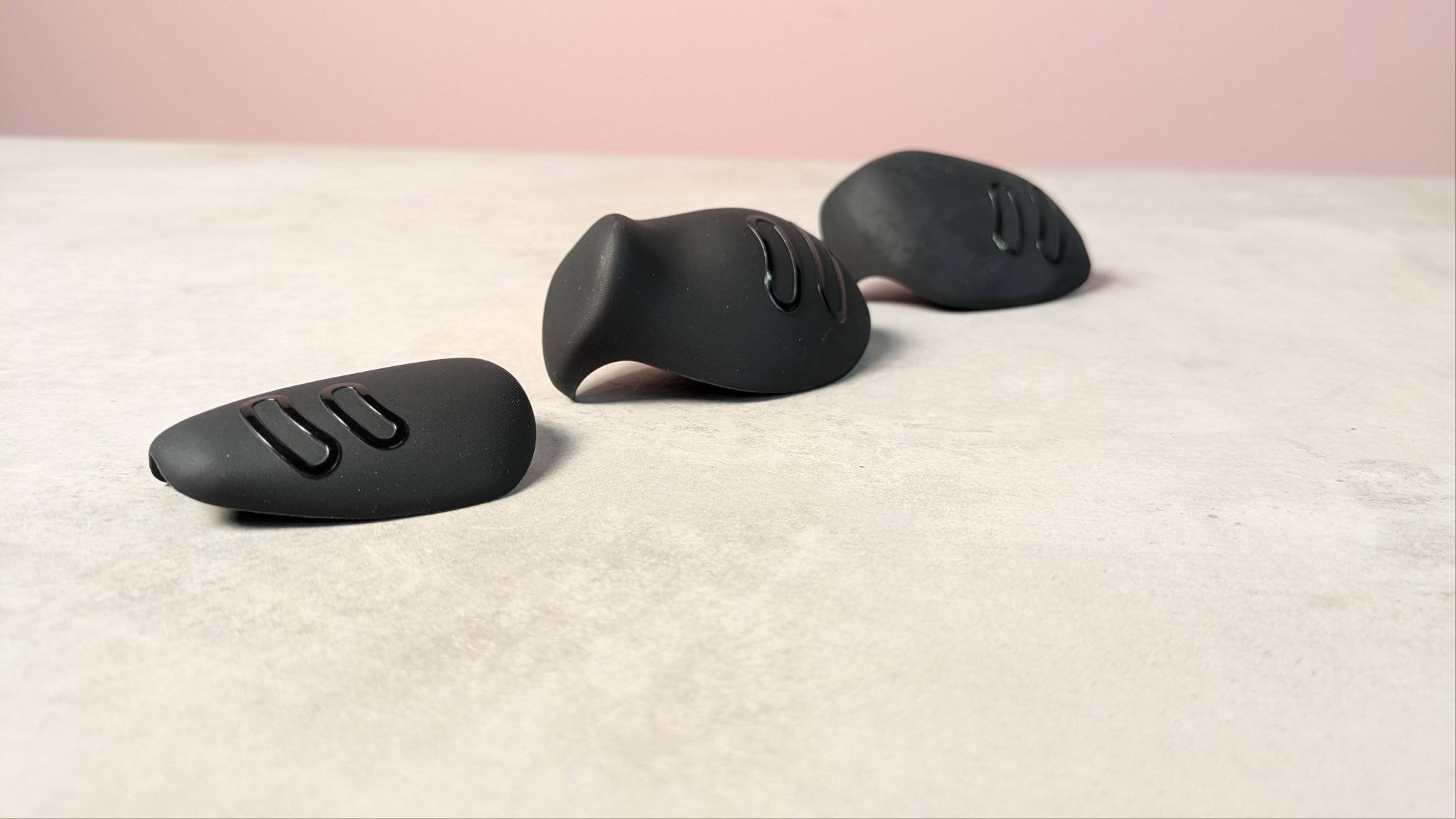 Three different grips of Genki Attack Vector, laid on table with pink wall in background