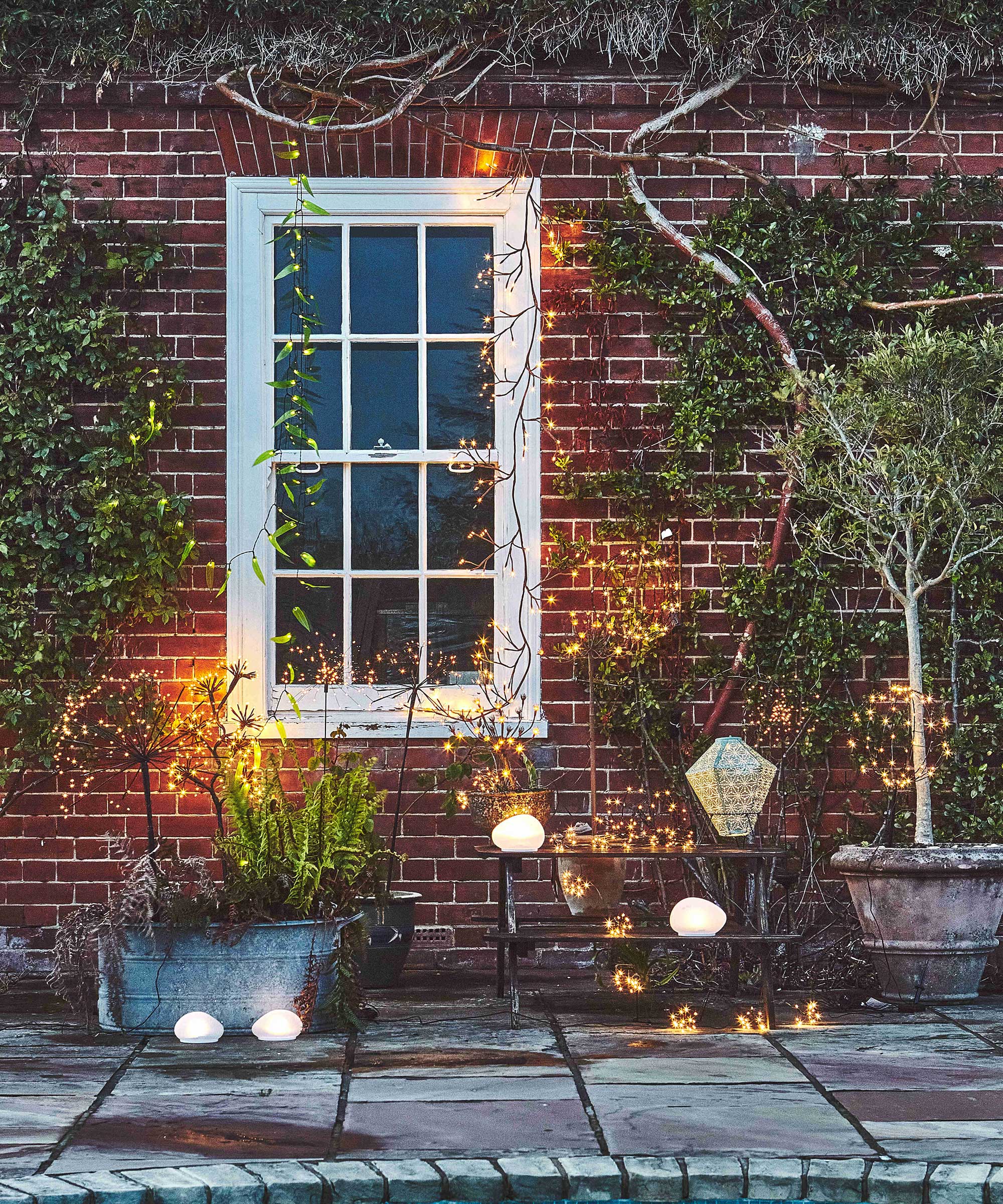 traditional brick house at dusk with paved outdoor patio area featuring planters and garden lighting