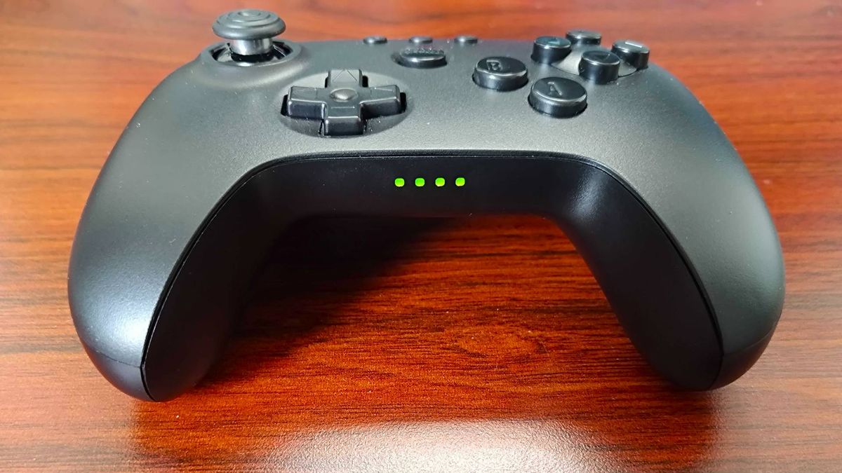 Bottom view 8Bitdo N64 Bluetooth controller with connection status lights glowing green on woodgrain surface.