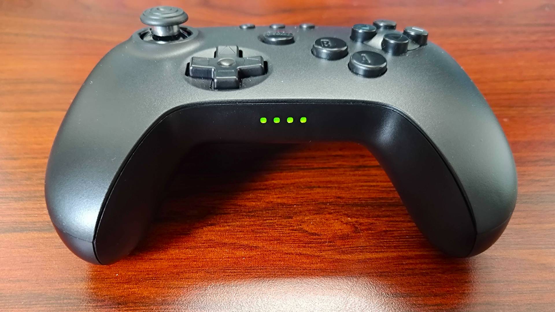 Bottom view 8Bitdo N64 Bluetooth controller with connection status lights glowing green on woodgrain surface.