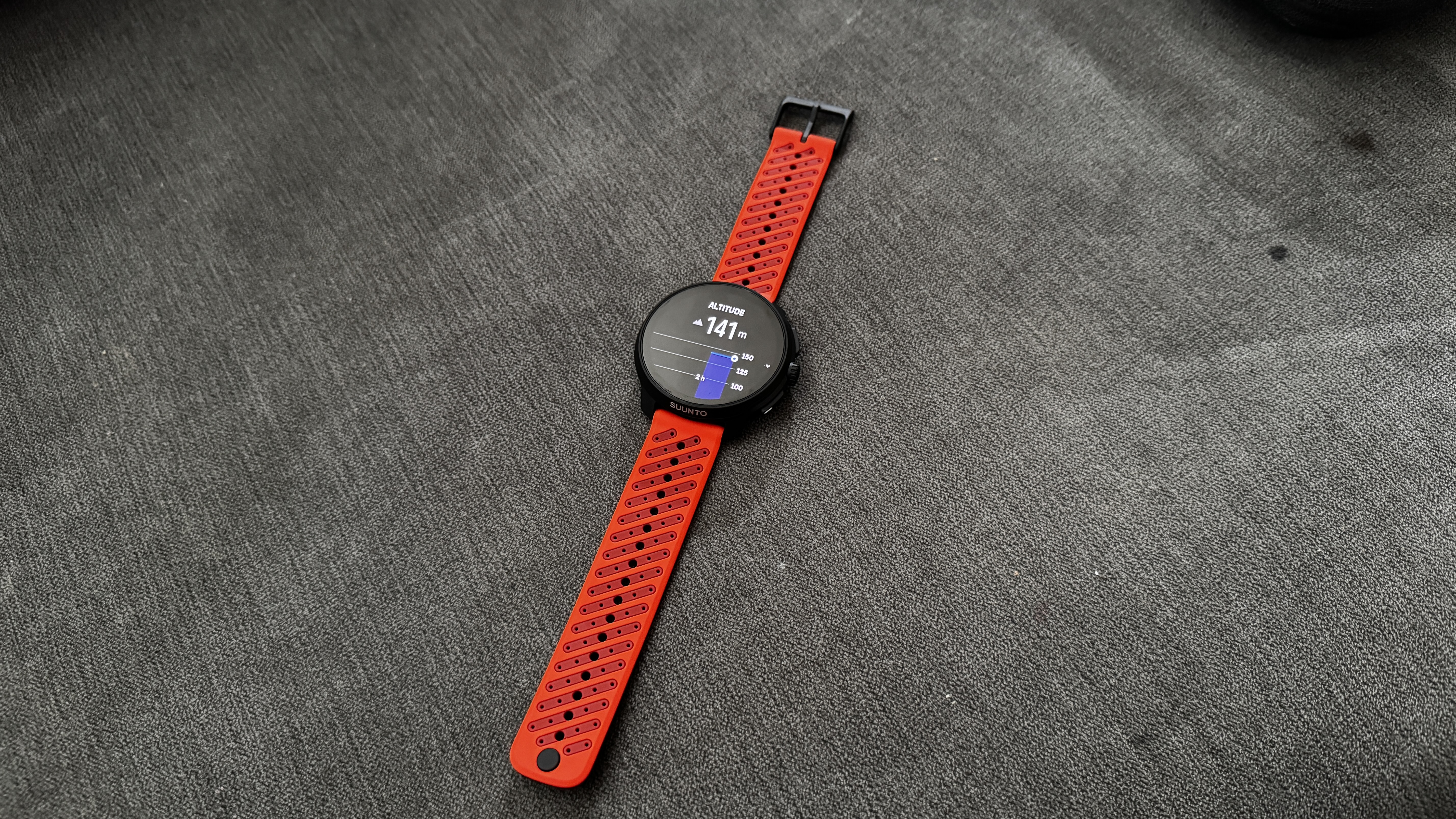 The Suunto Race 2 watch laying flat in a surface with an orange silicone wrist strap