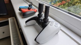 A DualSense and a pair of Nintendo Joy-Cons on a windowsill with Thumb Soldier attachments on both