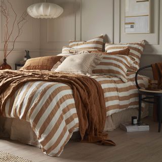 A bed with orange and white striped bedding and valance in a room with a neutral colour scheme