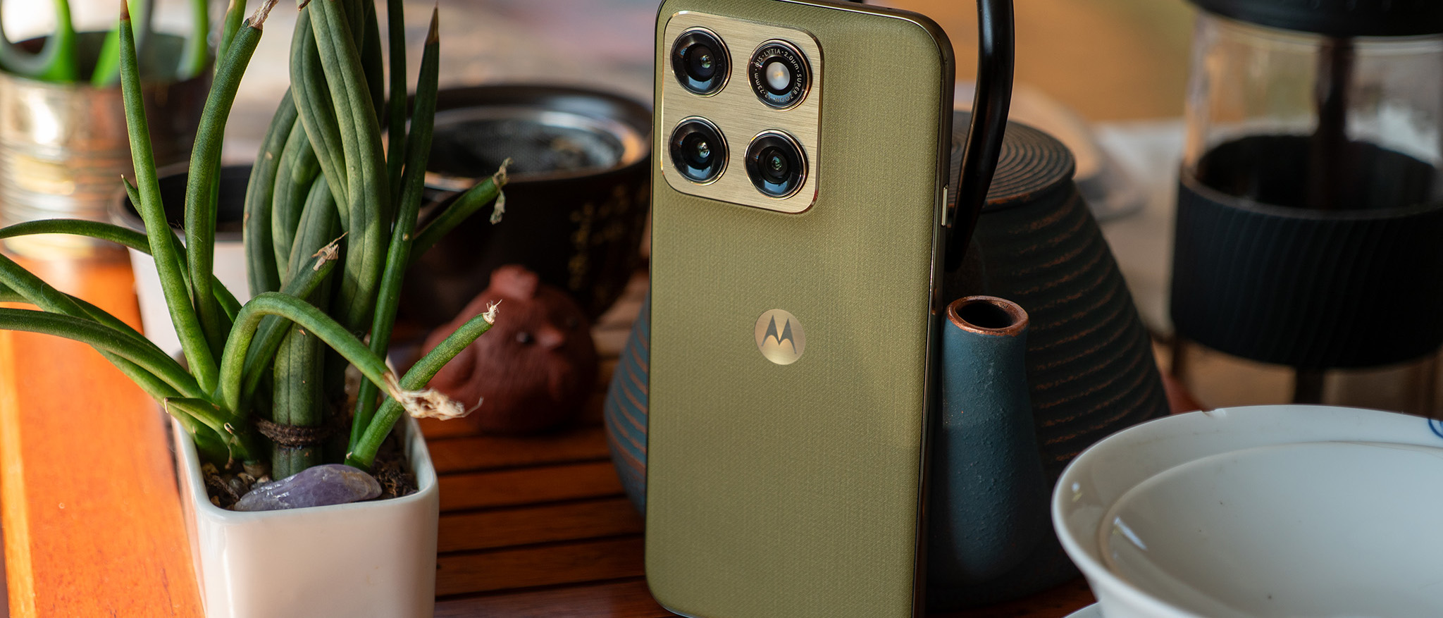 The back of the olive green Motorola Edge 2026 on a tea table next to a potted plant