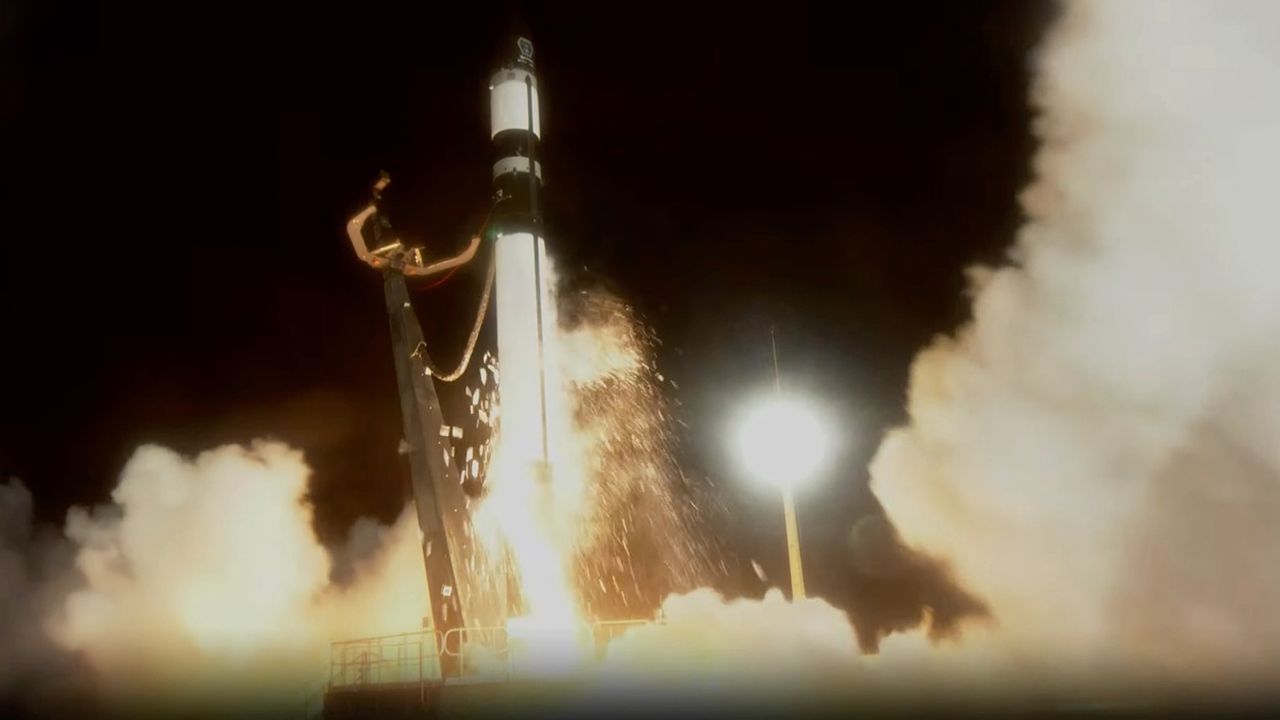 A white and black Rocket Lab Electron rocket launches into the nighttime sky with sparks spitting out from it on Feb. 18, 2024.
