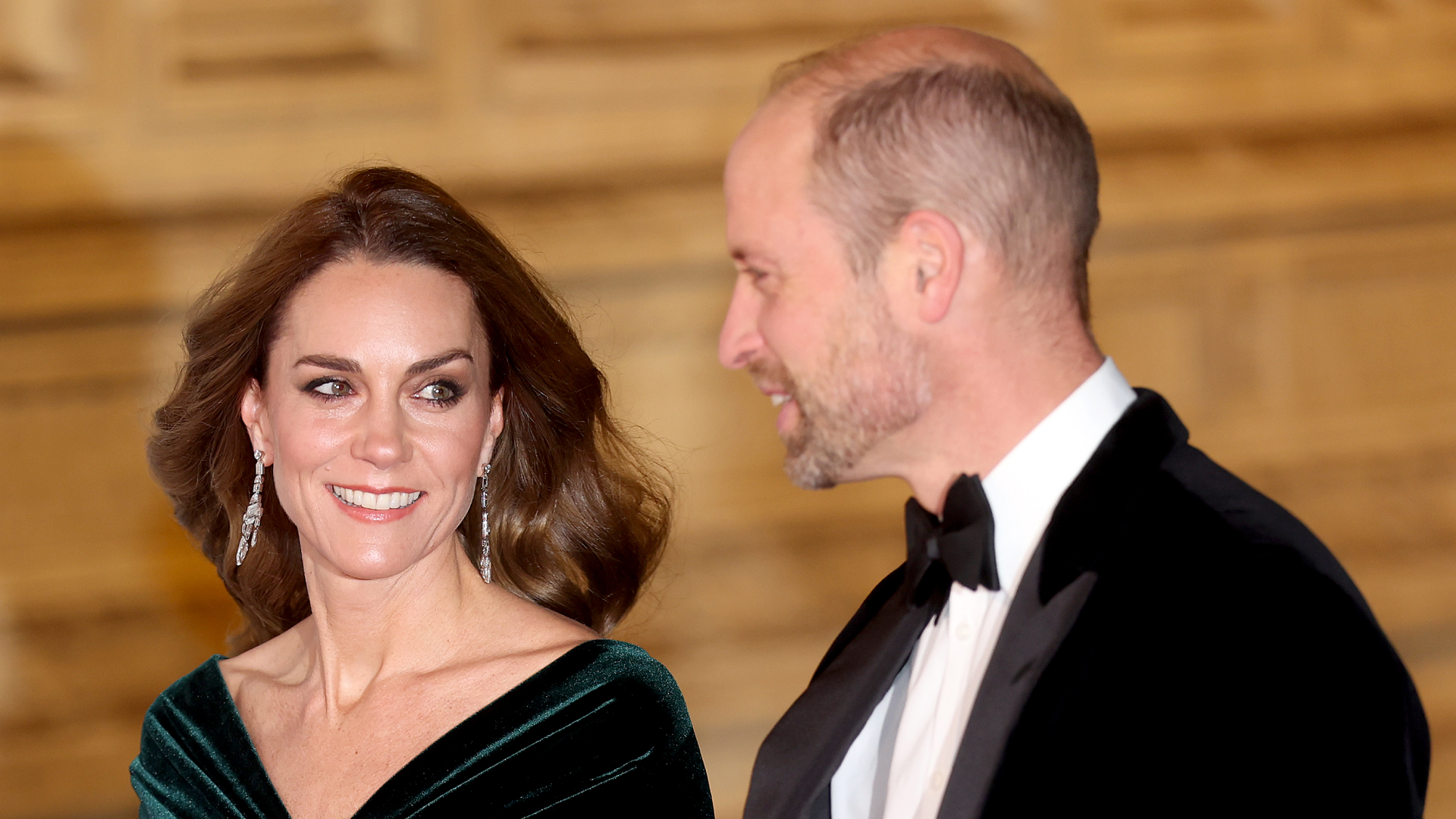 Prince William in a tux and Kate Middleton in a green gown smiling at the Royal Variety Performance