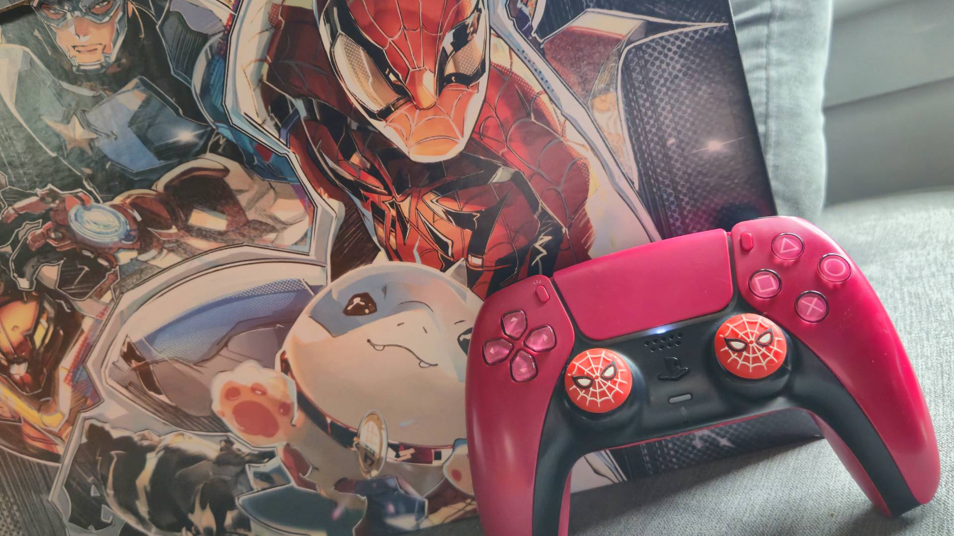 Photo by Rosalie Newcombe of a red PS5 controller with Spider-man stick grips sitting infront of an official Marvel Rivals comic box.