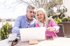 Mature couple looking at laptop sitting outside at a cafe.