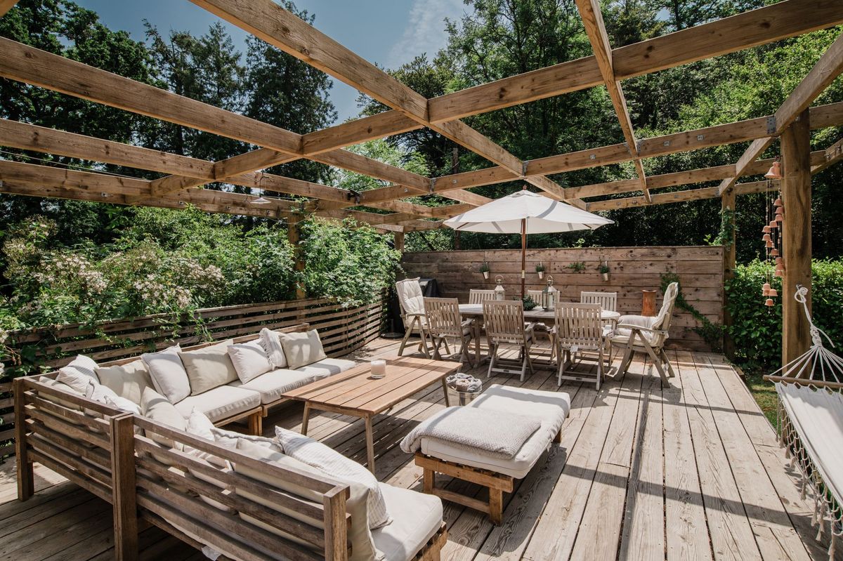 A timber pergola with sofa and dining table overlooking the forest