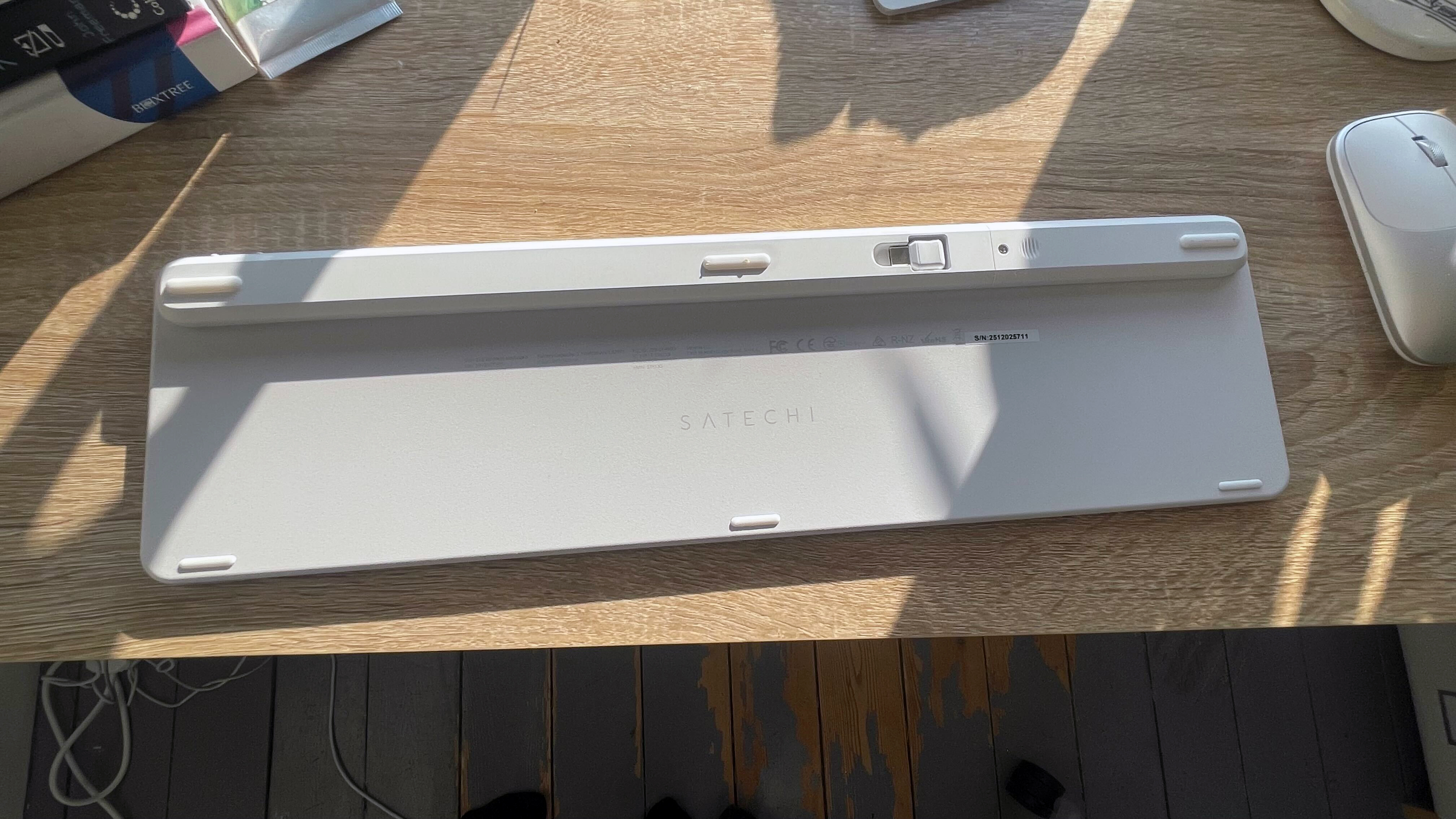 A silver grey Satechi Slim EX3 keyboard and Slim EX mouse on a wooden desk with sunlight shining on it from a window in the background