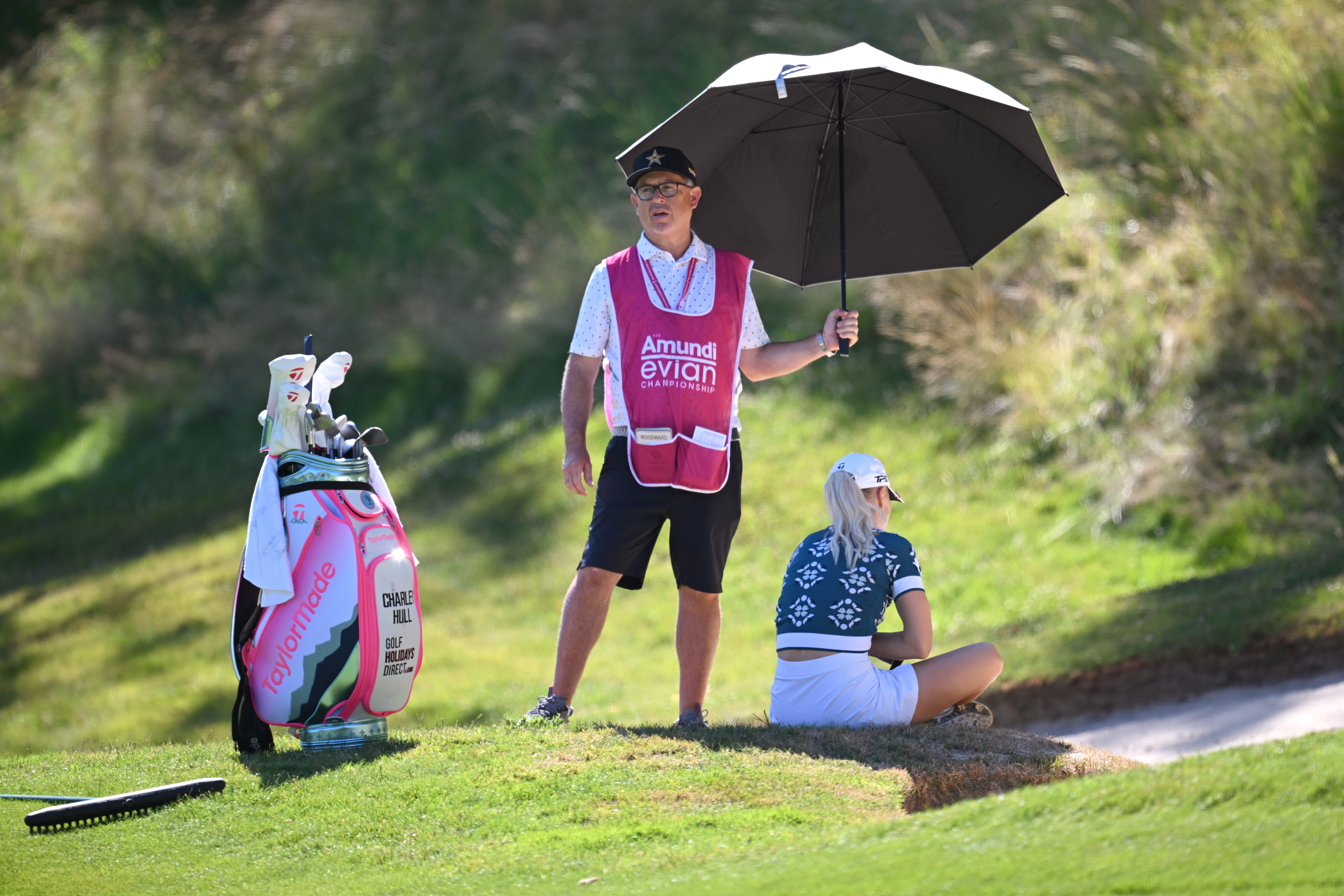 Charley Hull sits by a bunker at the Evian Championship as her caddie holds an umbrella over her for shade